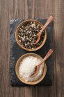 Black and white pepper and coarse sea salt with spoons in small bowls — Stock Photo