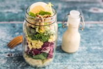 Orzo pasta with lambs lettuce, radicchio, endive, croutons, cheese, walnuts and eggs in a glass jar with dressing and a wooden fork — Stock Photo