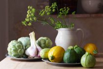 Una naturaleza muerta con calabacines redondos, ajo y alcachofas - foto de stock