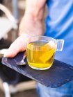Une personne servant une tasse de thé vert sur une planche d'ardoise — Photo de stock