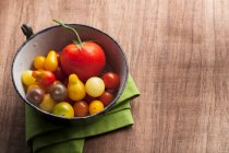 A variety of tomatoes in an antique enamel bowl on wood background with a green napkin — Stock Photo