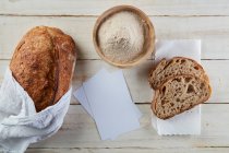 Tavolo in legno con un pane sourdogh, due fette di pane e un po 'di farina. — Foto stock