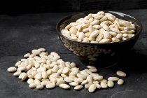 Dried white beans in a bowl and on a black surface — Stock Photo