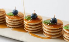 Several piles of mini pancakes with maple syrup, blueberries and mint — Stock Photo