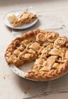 Torta de maçã com massa reticulada e rosas de pastelaria em assadeira, porção cortada no fundo — Fotografia de Stock
