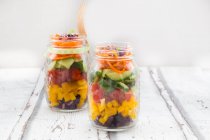 Ensalada arco iris en frascos de vidrio con col roja, pimiento amarillo, tomate, pepino, zanahorias y brotes de remolacha - foto de stock