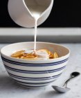 Milch wird auf eine blau-weiße Schüssel mit Mini-Pfannkuchen Müsli gegossen — Stockfoto