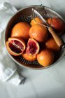 Cut and whole Blood oranges in rustic metal colander — Stock Photo