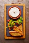 Baked cheese with toasted bread and vegetables on board — Stock Photo