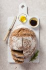 Un pain au levain tranché servi sur une planche à découper en céramique blanche avec de l'huile d'olive et du vinaigre balsamique — Photo de stock