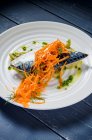 Filete de pescado de caballa azul con berenjenas y zanahorias rociadas con aceite de oliva y adornadas con eneldo y hierbas en un plato blanco - foto de stock