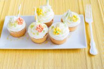 Springtime cupcakes with sugar flowers on plate and fork on yellow table setting — Stock Photo