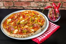 Pizza elaborada con masa fermentada, salsa de tomate con orégano y aceite de oliva, queso mozzarella, pimientos verdes, amarillos y rojos, salami picante y pepperoni - foto de stock