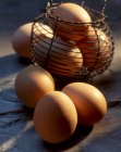 Frische Bauernhof-Eier auf Steinoberfläche und im Mini-Drahtkorb — Stockfoto