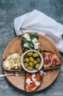 Various bruschettas and olives on a wooden plate — Stock Photo