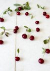 Fresh cherries with green leaves on white stone surface — Stock Photo