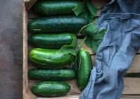 Freshly harvested cucumbers (cucumis sativus) with leaves in a wooden crate — Stock Photo