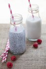 Chia seeds with almond milk in bottles and raspberries on table — Stock Photo