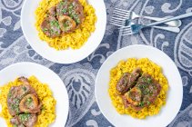 Three portions of osso buco milanese meat on a yellow saffron risotto garnished with fresh chopped parsley — Stock Photo