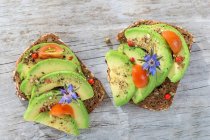 Wholegrain bread topped with avocado slices, tomato and borage flowers — Stock Photo