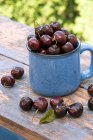 Fresh cherries in enamel cup and on rustic wooden table — Stock Photo