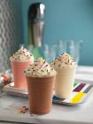 Три різні молочні коктейлі з вершками та барвистими цукровими зморшками — стокове фото