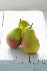 Three green pears on a white wooden background — Stock Photo