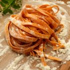 Roasted red pepper pasta on dough board with flour — Stock Photo