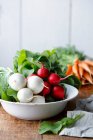 Radishes and carrots in a bowl, with carrots in the background — Stock Photo