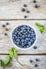 Blueberries in white bowl and on table with leaves — Stock Photo