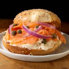 Salmon and cream cheese on sesame bagel with capers and red onions — Stock Photo