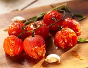 Tomates vermelhos frescos com alecrim e alho na mesa de madeira — Fotografia de Stock