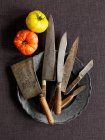 Various vintage knives on pewter plate and tomatoes on table — Stock Photo