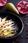 Pear and endive salad with pomegranate seeds in a black plate on black background — Stock Photo