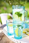 Beber com limão e hortelã em copos e jarro no fundo — Fotografia de Stock