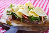 A slice of crusty bread topped with gouda, figs and rocket — Stock Photo