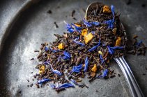 Hoja suelta Earl Grey té con cáscara de cítricos secos de limón, naranja y bergamota y acianos azules en un plato de metal oscuro y una cucharadita - foto de stock
