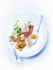 Бекон і рибне філе зі смаженою картоплею та огірком на тарілці з столовими приборами — стокове фото