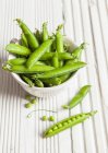 A white bowl full of fresh peas in their pods — Stock Photo