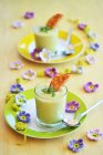 Sopa de aguacate en dos vasos con tostadas y berro fresco, y flores decorativas de primavera de ganchillo - foto de stock