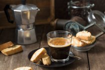 Espresso en una copa y cantuccini con una cafetera estufa en el fondo - foto de stock