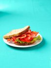 Specksalat und Tomatensandwich auf Teller auf blauem Hintergrund — Stockfoto