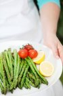 A woman holding a plate of grilled green asparagus — Stock Photo