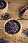 Black rice in wooden bowls with scoop on rustic wooden surface — Stock Photo
