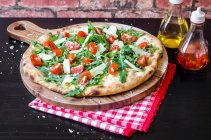 Pizza feita com uma base de massa, folhas de foguete fresco, tomates cereja e queijo parmigiano em uma placa de madeira — Fotografia de Stock