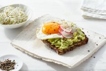 Dark rye bread topped with avocado, a fried egg, radishes and sprouts — Stock Photo
