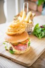 Bacon cheese beef burger with gherkins, pickle, tomato, fresh salad, bacon, cheese and fried onion rings ona wooden board with chips and salad — Stock Photo