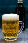 Helles Bier im Glas mit Schaum und Flasche auf Hintergrund — Stockfoto