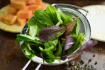 Ingredientes de salada: folhas mistas que se lavam em uma peneira — Fotografia de Stock