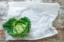 A savoy cabbage on paper and a wooden background (top view) — Stock Photo
